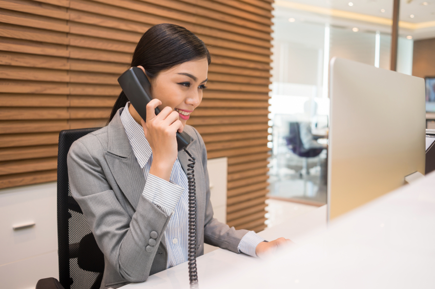 Pretty Vietnamese receptionist talking on telephone at her workplace